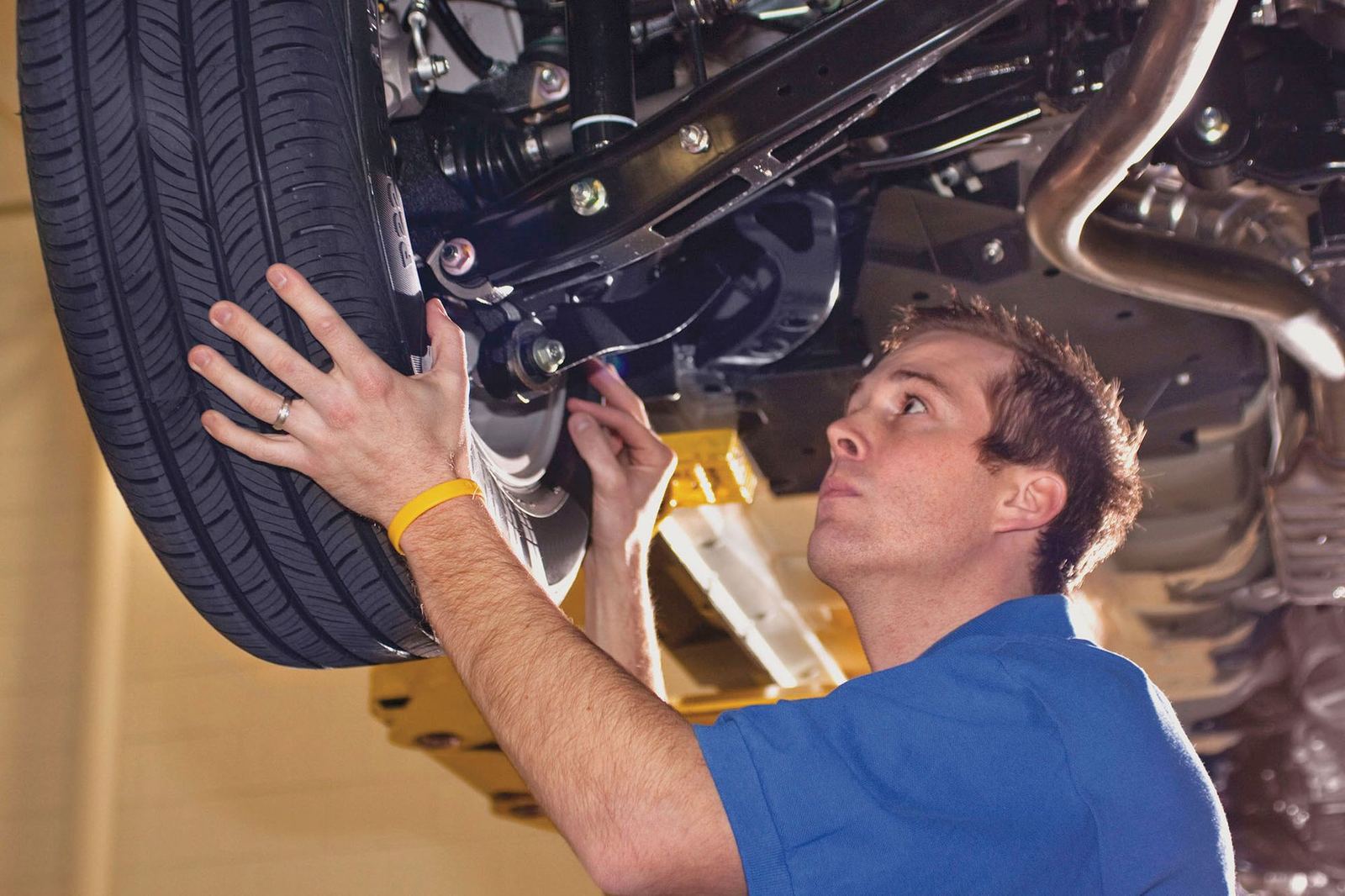 Mechanic inspecting a vehicle's tire and suspension from below